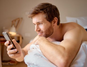 Attractive male on bed swiping through an hookup app on his mobile phone