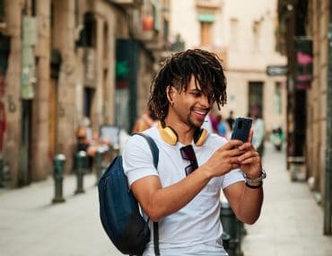black man with dreadlocks holding up his phone in the middle of the street