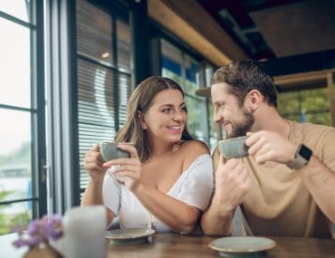 Long haired woman and bearded man smiling at each other during a cafe date