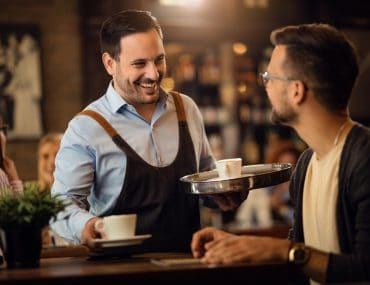 A waiter offering a customer a cup of coffee in a cafe