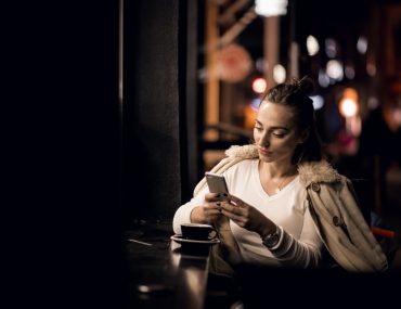Woman wearing a jacket and sitting at a lounge counter, using her phone