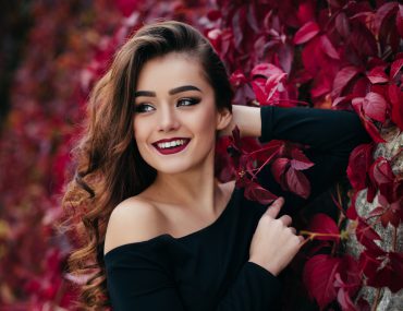 Pretty girl wearing a black dress standing beside a flower-tree