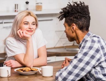 Interracial couple staring lovingly at each other with cookies and a cup on the table